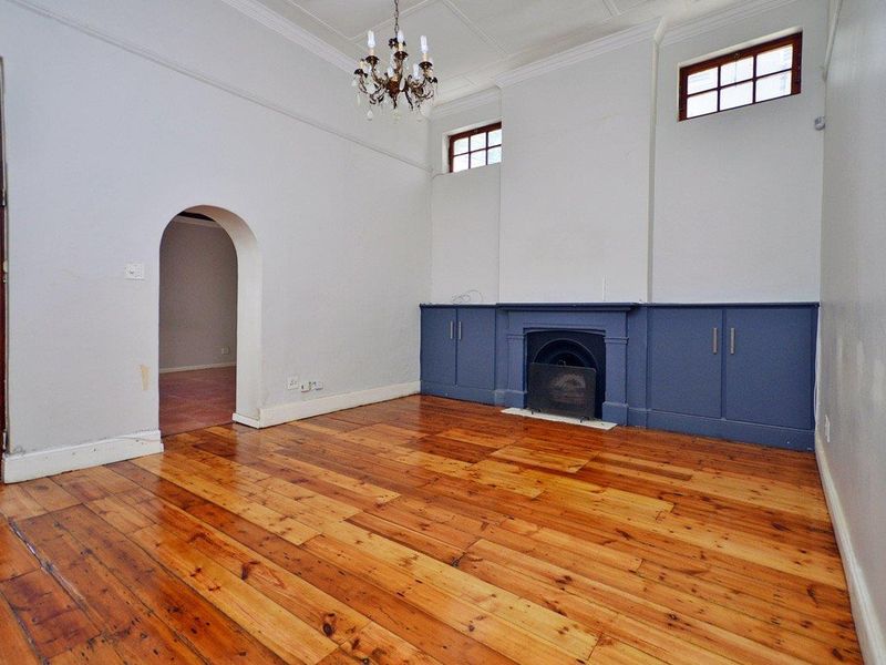Spacious living room featuring polished hardwood floors, a classic fireplace with built-in cabinetry, an elegant archway, and high ceilings with crown molding.