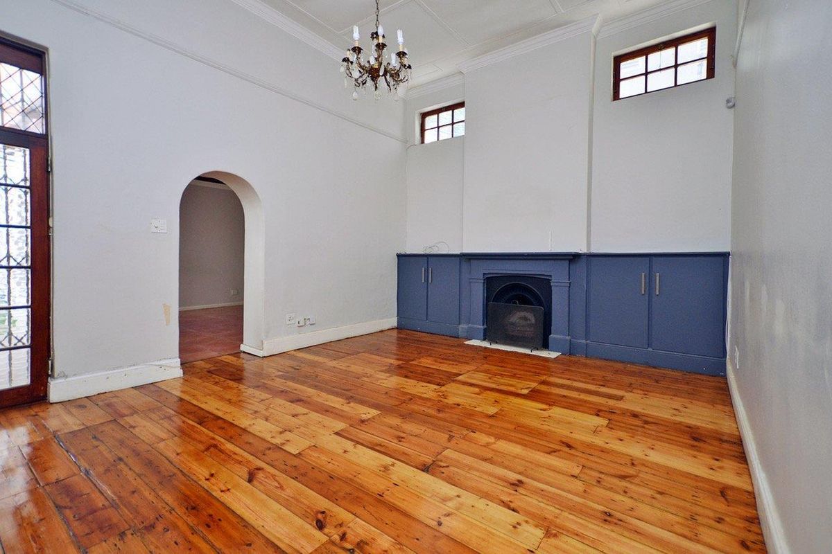 Spacious living room featuring polished hardwood floors, a classic fireplace with built-in cabinetry, an elegant archway, and high ceilings with crown molding.