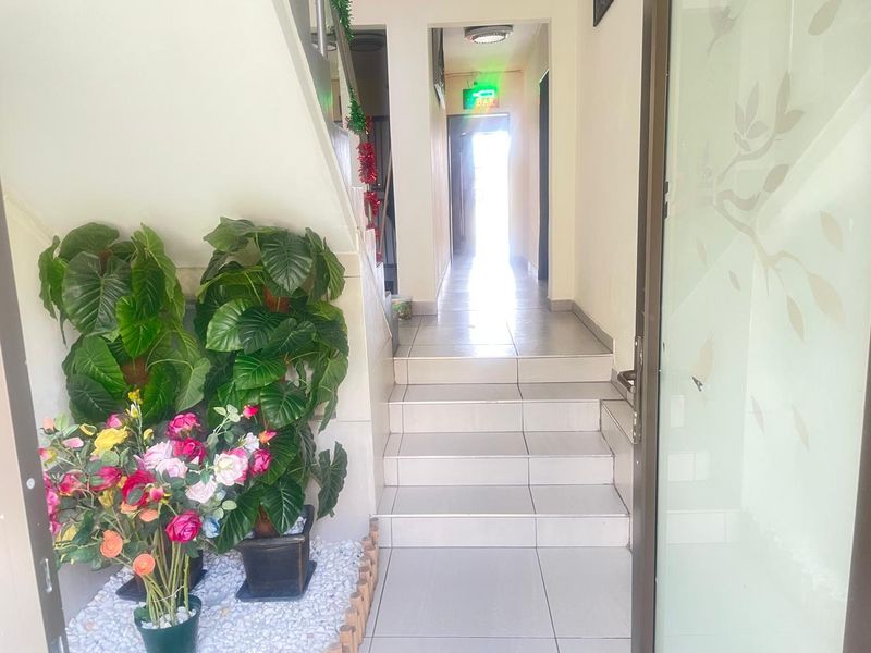 A tiled interior hallway featuring a staircase leading to an upper level, with a clear view towards a rear exit.