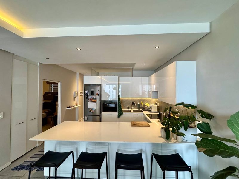 Modern open-plan kitchen featuring sleek white cabinetry, a spacious stone island, integrated appliances, and recessed lighting, creating a functional and contemporary living space.
