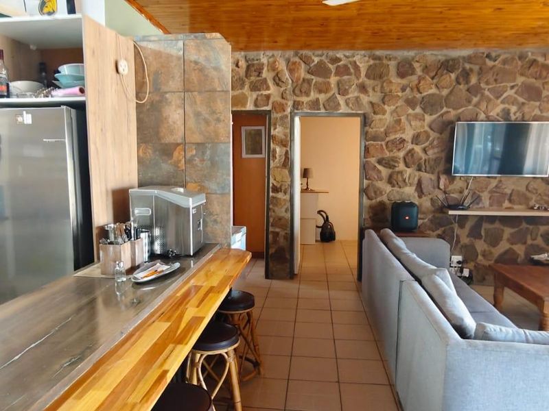 Open-plan living and kitchen area featuring a rustic stone feature wall, timber ceiling, tiled flooring, and a functional breakfast bar.