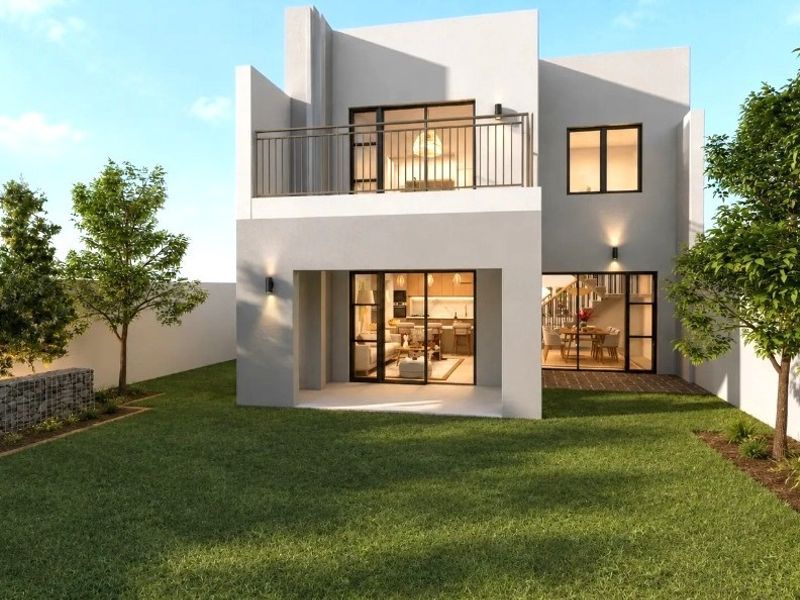 Rear view of a modern two-story house featuring a private garden, a ground-floor patio, and an upper-level balcony with metal railings.