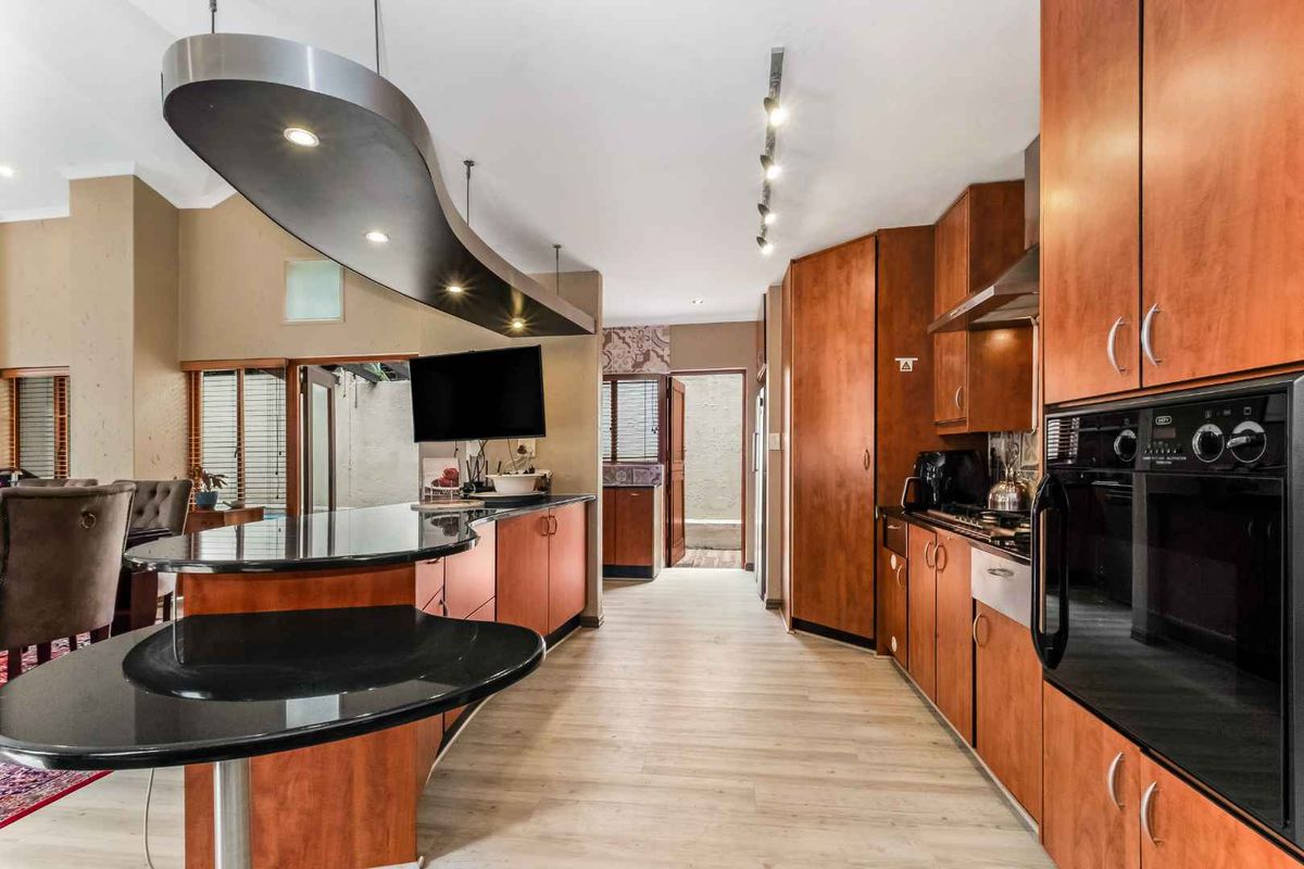 Spacious kitchen featuring wood-finish cabinetry, black granite countertops, a unique curved breakfast bar, and built-in oven and hob.