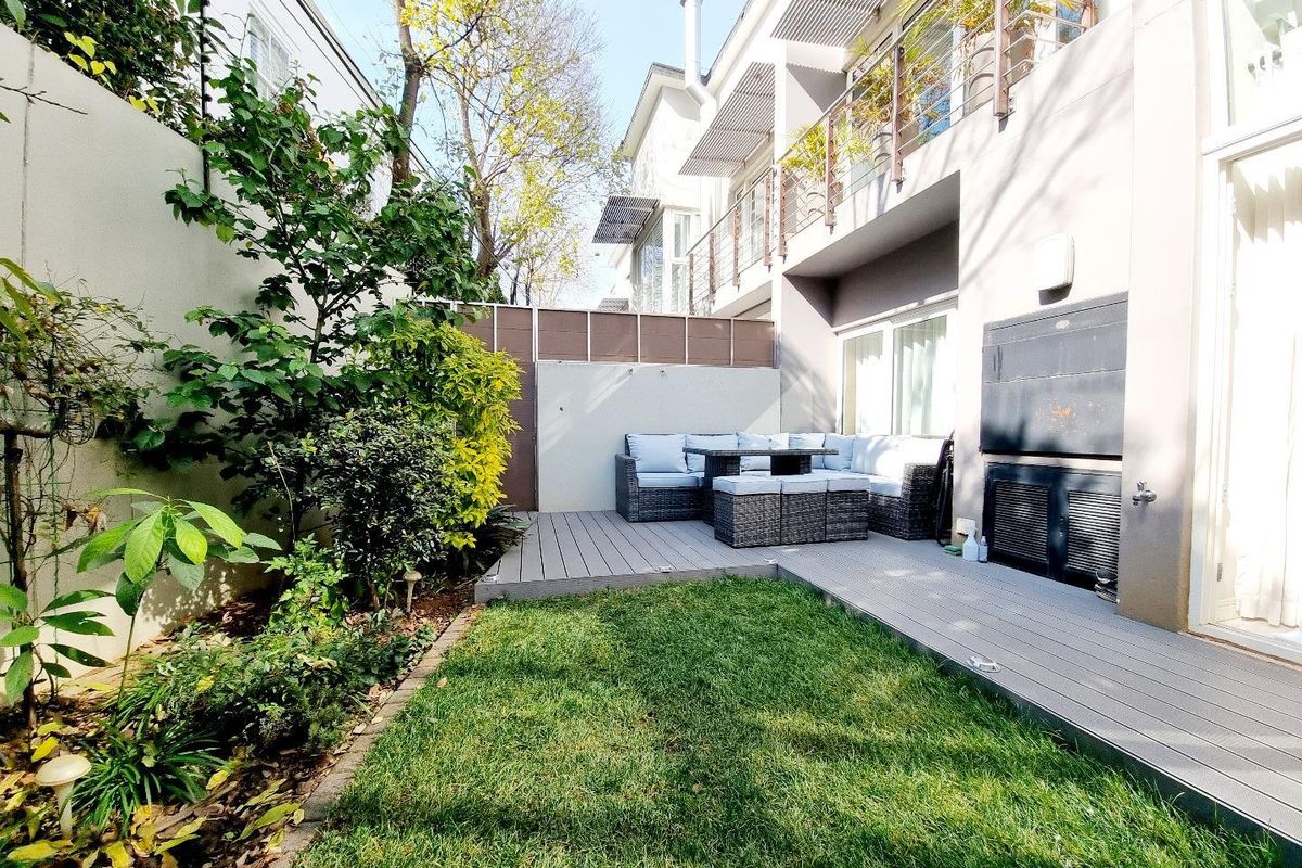 A private rear garden featuring a composite timber deck, built-in braai area, and landscaped lawn, providing a functional outdoor entertainment space.
