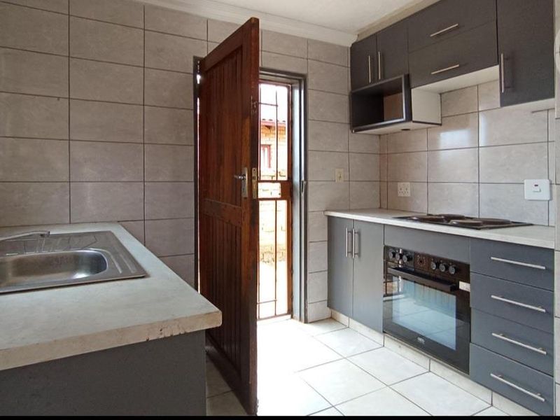 A functional kitchen featuring modern grey cabinetry, built-in oven and hob, stainless steel sink, and neutral tiled finishes throughout.