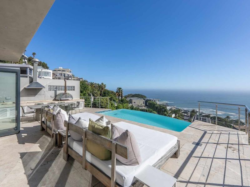 Expansive outdoor terrace featuring an infinity pool, built-in fireplace, pizza oven, and stunning coastal ocean views.