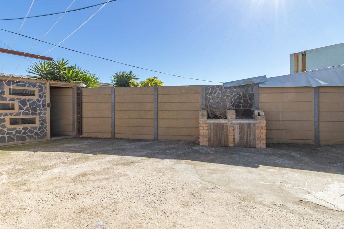 A rear courtyard area featuring a built-in braai, concrete paving, and precast boundary walls, offering a functional outdoor space in need of maintenance.