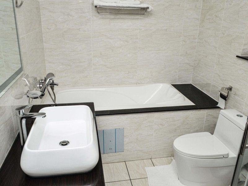 A compact, modern bathroom featuring a built-in bathtub, vessel sink vanity, and neutral tiled finishes throughout.