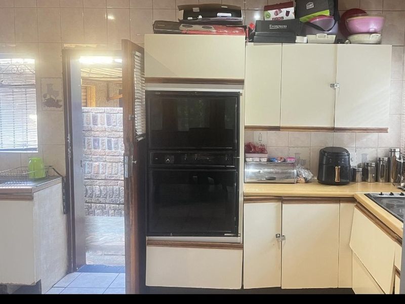 A dated kitchen featuring built-in cabinetry, a wall-mounted oven, and tiled backsplash, with direct access to an outdoor area.