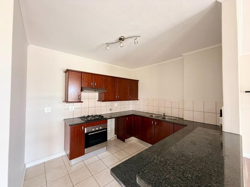 A functional kitchen featuring dark wood cabinetry, granite countertops, a built-in oven with gas hob, and a double bowl sink with tiled backsplash.