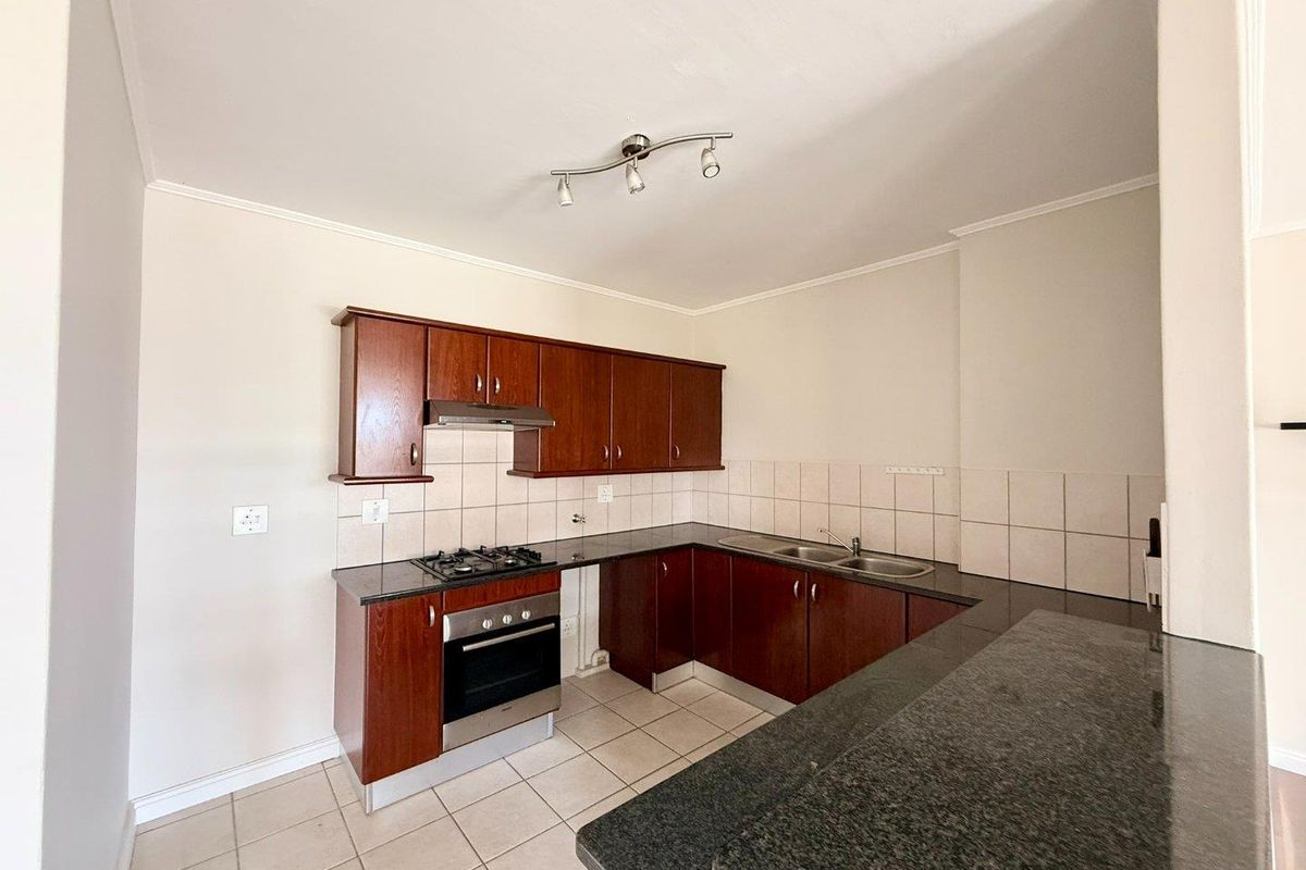 A functional kitchen featuring dark wood cabinetry, granite countertops, a built-in oven with gas hob, and a double bowl sink with tiled backsplash.