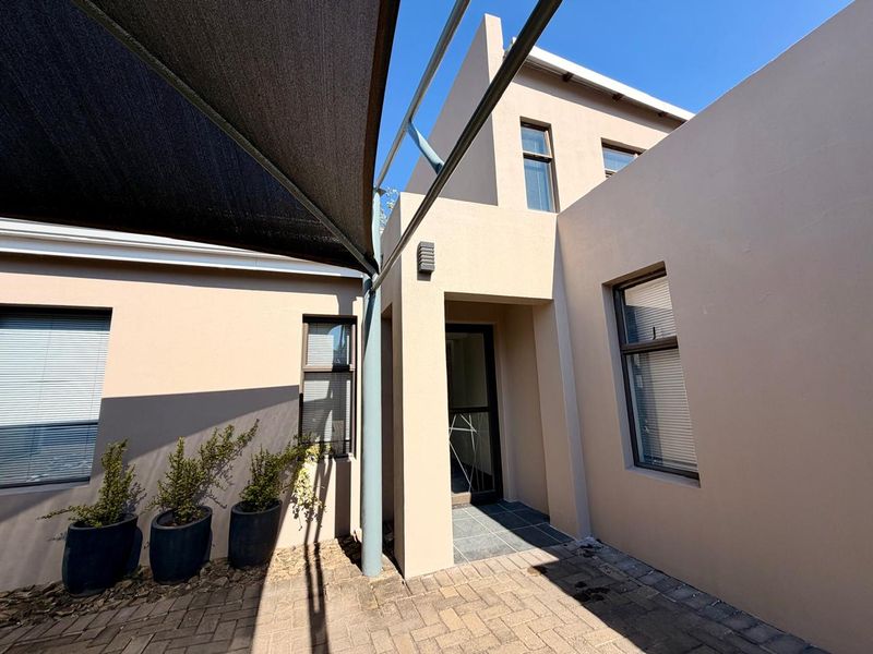 A well-maintained rear courtyard featuring paved flooring, a modern shade sail, and clean exterior finishes with aluminium window frames.