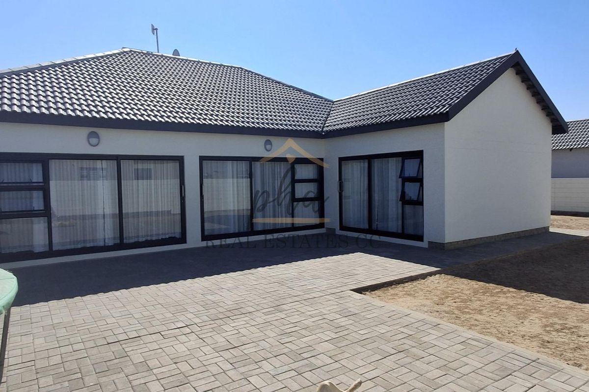 Rear view of the property featuring a paved patio area, modern tiled roof, and large sliding glass doors providing access to the interior.