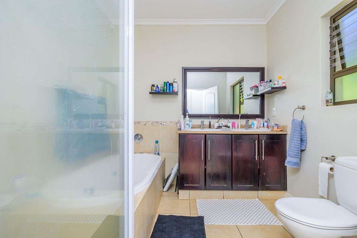 A functional bathroom featuring a dark wood vanity with dual basins, a built-in bathtub, a glass shower enclosure, and a wall-mounted mirror.