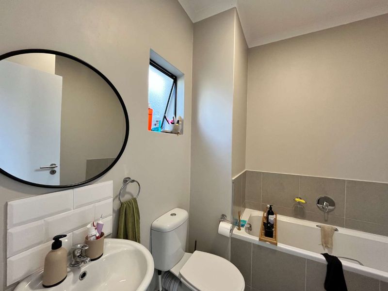 A clean, functional bathroom featuring a pedestal basin, toilet, and a tiled bathtub area with neutral finishes and natural light.