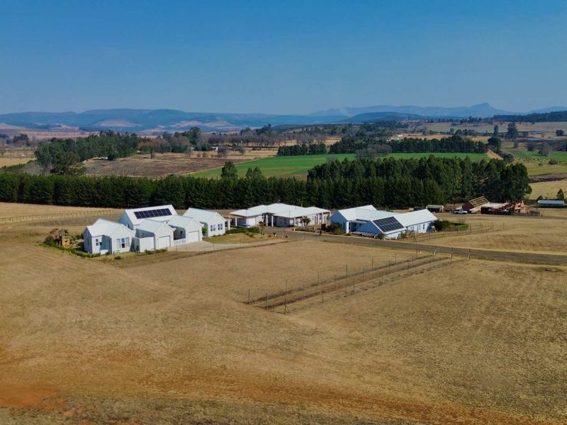 Aerial view of a residential property featuring multiple buildings with metal roofs, solar panels, and expansive surrounding rural land.