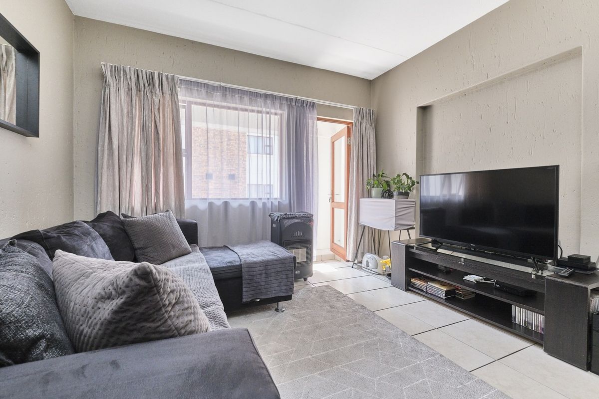 A comfortable living room featuring tiled flooring, a large window for natural light, and direct access to an outdoor area via a glass door.