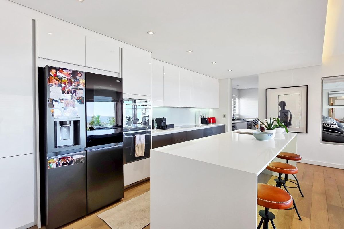 Modern kitchen featuring sleek white glossy cabinetry, a large central island with quartz countertops, integrated appliances, and warm hardwood flooring.