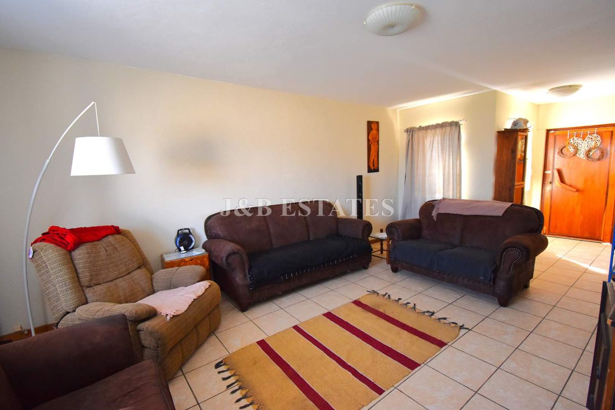A spacious living room featuring neutral tiled flooring and a simple ceiling light fixture, providing a functional and comfortable living area.