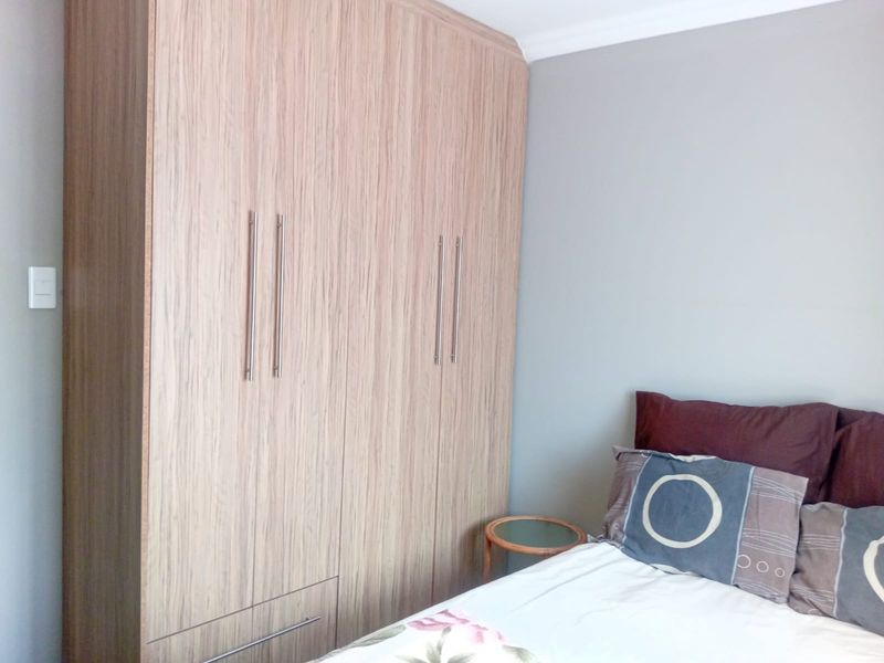 A bedroom featuring modern, light wood-grain built-in cupboards with sleek metal handles.