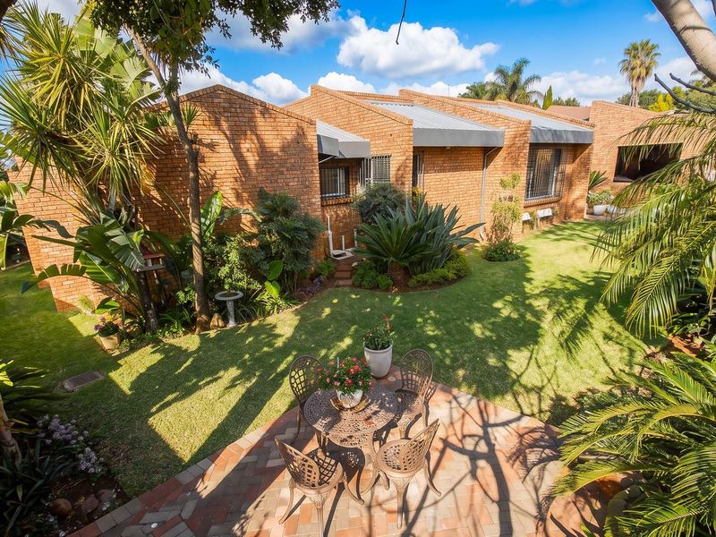 A well-maintained rear exterior view featuring a brick facade, metal roofing, a paved patio area, and a lush landscaped garden.