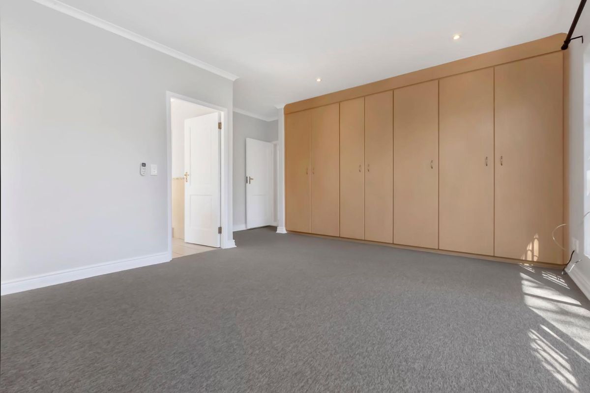 A spacious bedroom featuring neutral wall tones, grey carpeting, and extensive built-in wooden cabinetry for ample storage.