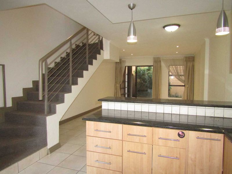Open plan living area featuring a kitchen with granite countertops, tiled flooring, and a staircase with a metal balustrade leading to the upper level.