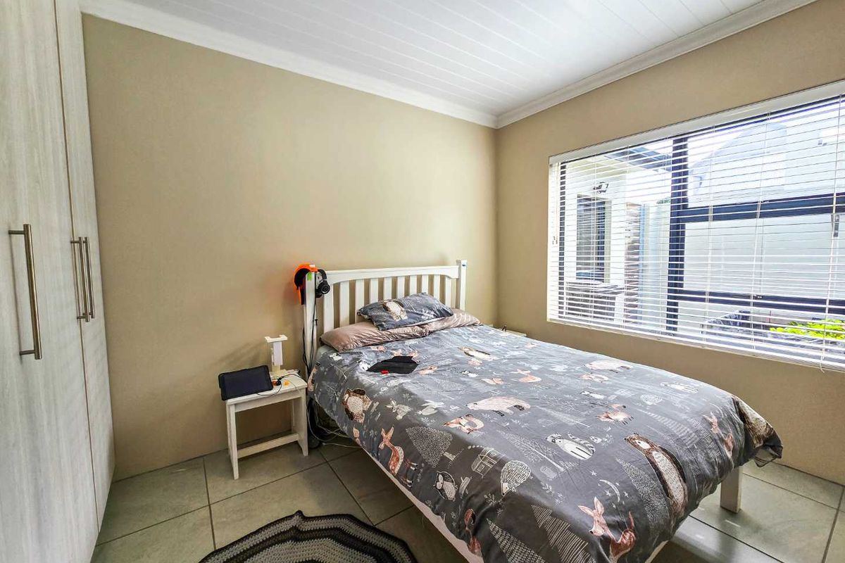 A functional bedroom featuring built-in cupboards, tiled flooring, and a large window with fitted blinds.