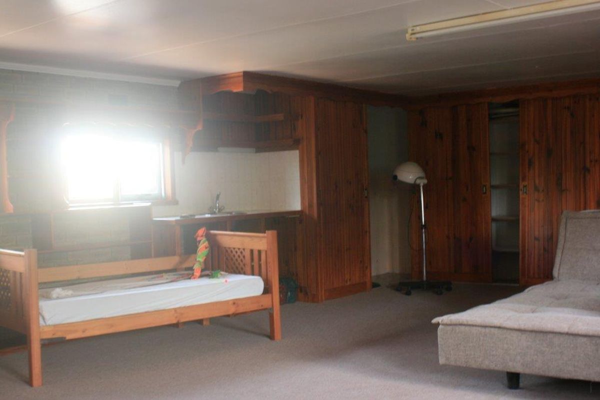 A spacious bedroom featuring extensive built-in timber cabinetry, integrated shelving, and a small kitchenette area with a sink.