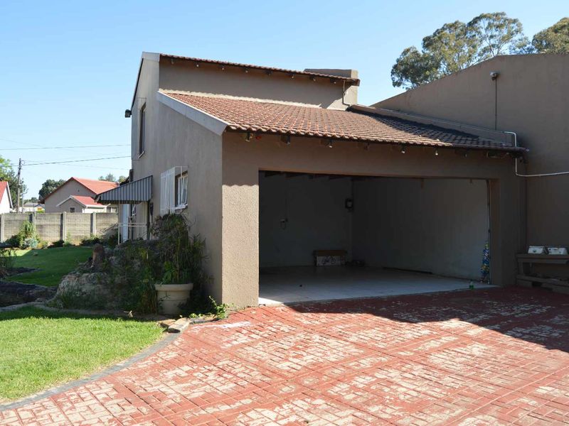 A detached garage with a tiled roof and paved driveway, featuring an open entrance and adjacent garden area.