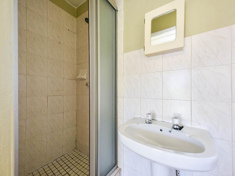 A compact bathroom featuring a shower enclosure, pedestal basin, and wall-mounted medicine cabinet, requiring cosmetic updates to the tiling and finishes.