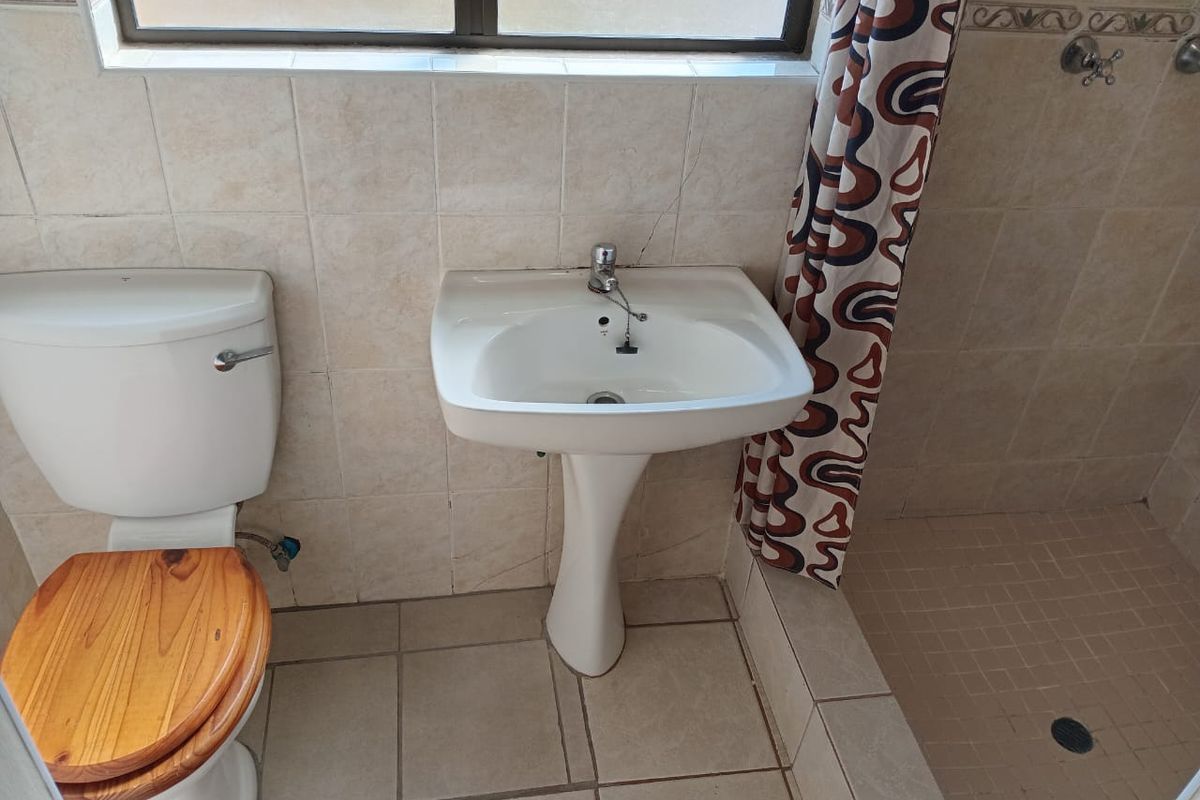 A functional bathroom featuring a pedestal basin, a standard toilet, and a tiled shower enclosure with a window for natural light.
