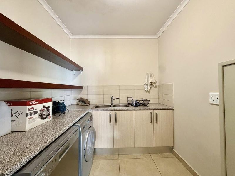 A functional laundry room featuring built-in cabinetry, a double bowl sink, laminate countertops, and tiled splashbacks with convenient floating shelving.