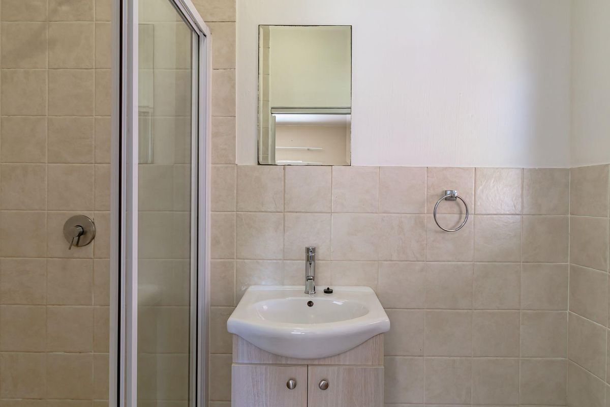 A functional bathroom featuring a shower enclosure, a vanity unit with a basin, and neutral wall tiling.