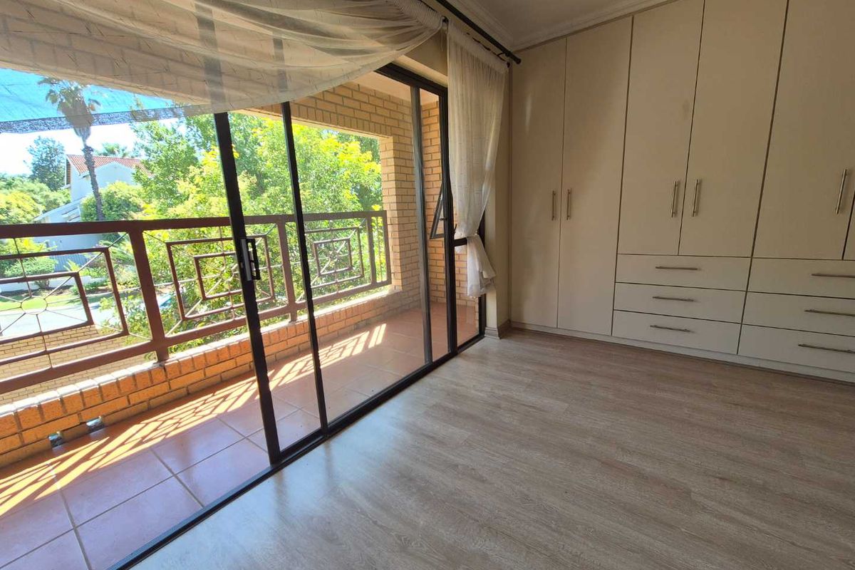 A bright bedroom featuring built-in cupboards, laminate flooring, and large sliding glass doors that open onto a private covered balcony.