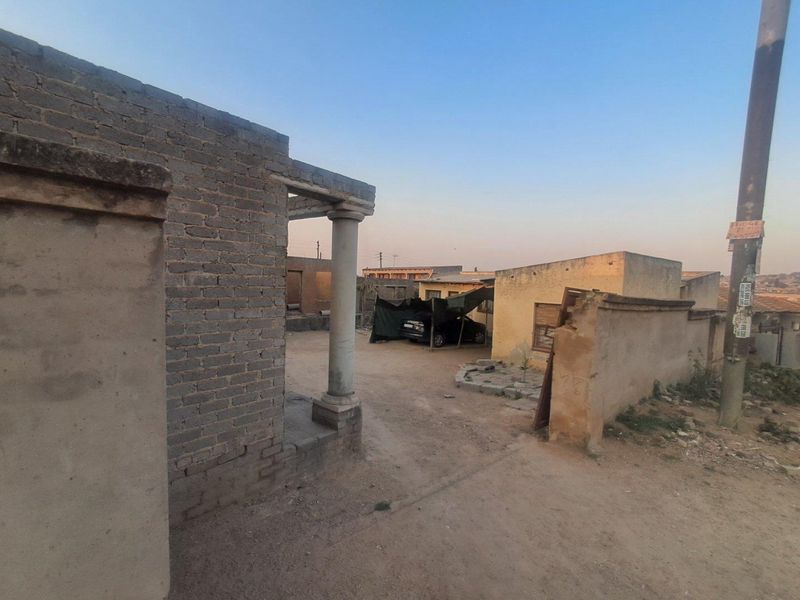 Exterior view of the property frontage featuring a brick boundary wall, concrete column, and an unpaved driveway area.