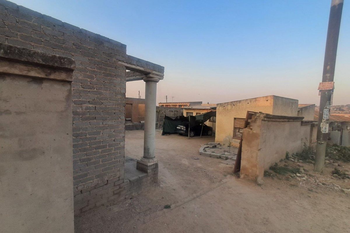 Exterior view of the property frontage featuring a brick boundary wall, concrete column, and an unpaved driveway area.