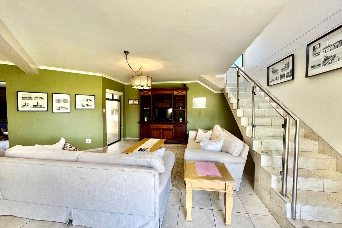 Spacious living room featuring tiled flooring, a built-in staircase with glass balustrades, and access to an adjacent outdoor area.