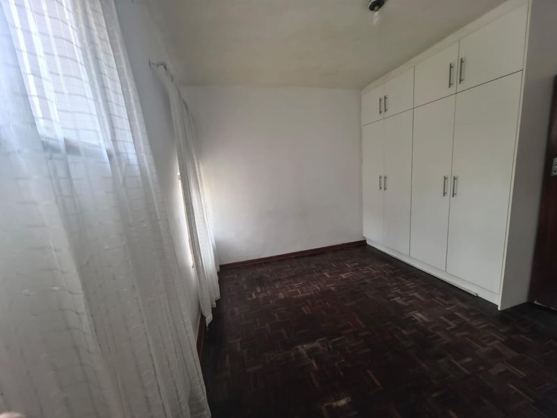 A vacant bedroom featuring dark parquet flooring and floor-to-ceiling built-in cupboards, offering a neutral canvas for personalization.