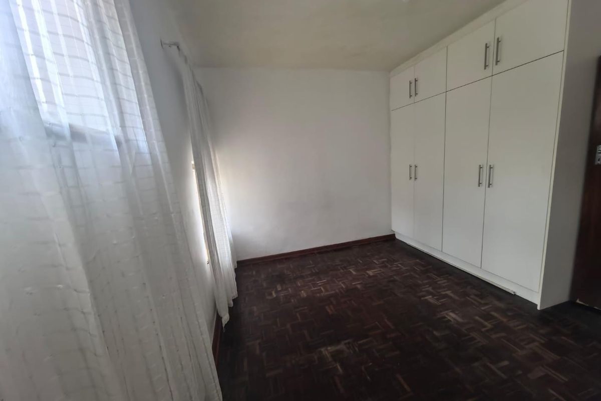 A vacant bedroom featuring dark parquet flooring and floor-to-ceiling built-in cupboards, offering a neutral canvas for personalization.