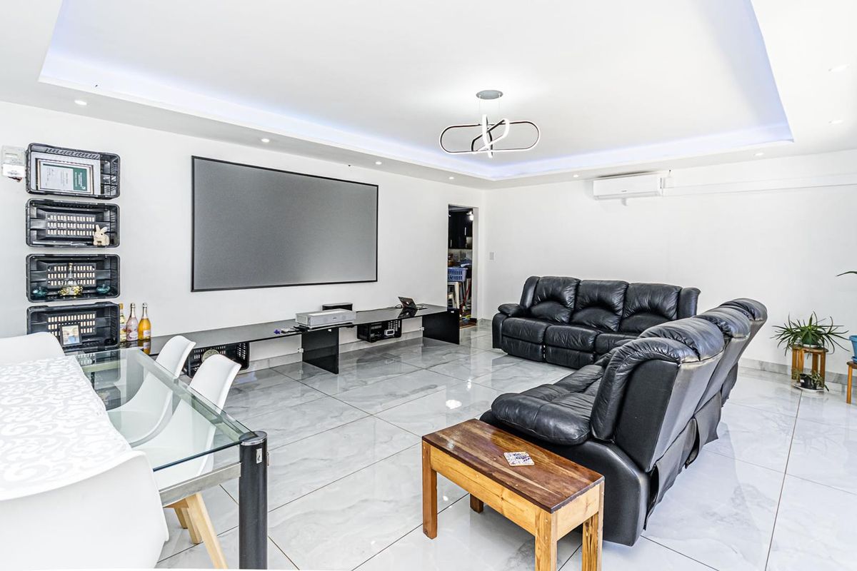 Spacious living area featuring modern porcelain floor tiles, recessed cove lighting, and a wall-mounted projector screen, creating a functional entertainment space.
