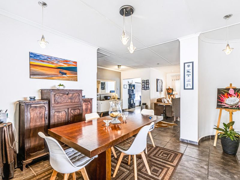 An open-plan dining area featuring tiled flooring, cove cornicing, and modern pendant lighting, flowing into an adjacent living space.