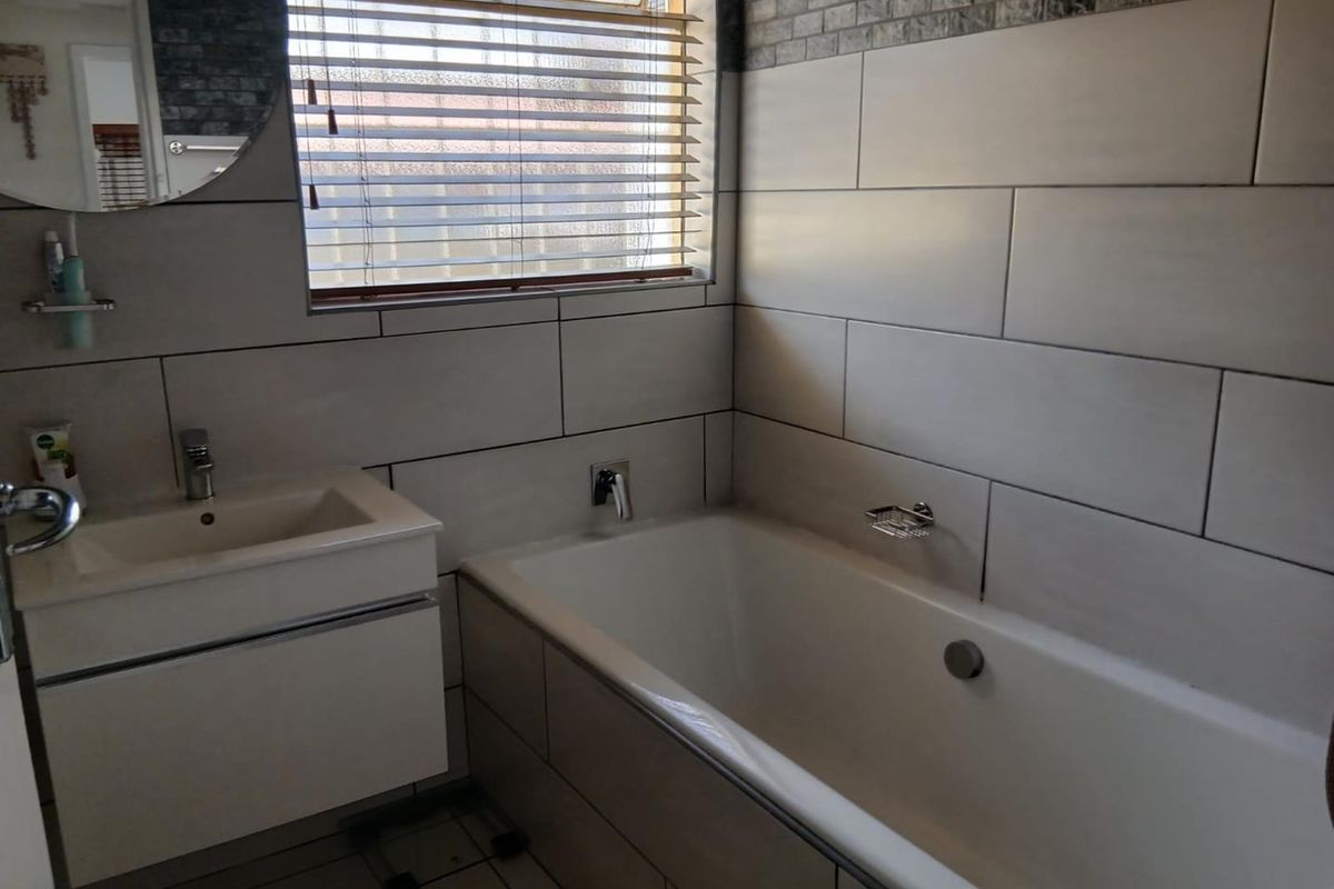 A modern bathroom featuring a built-in bathtub, wall-mounted vanity with basin, and contemporary tiled walls.