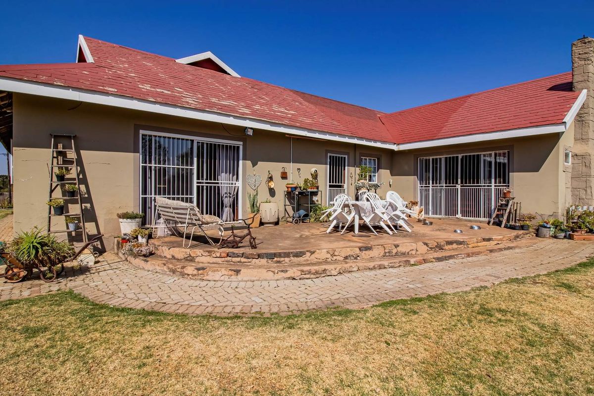 Rear view of the property featuring a paved patio area, stone chimney, and sliding door access to the main dwelling.