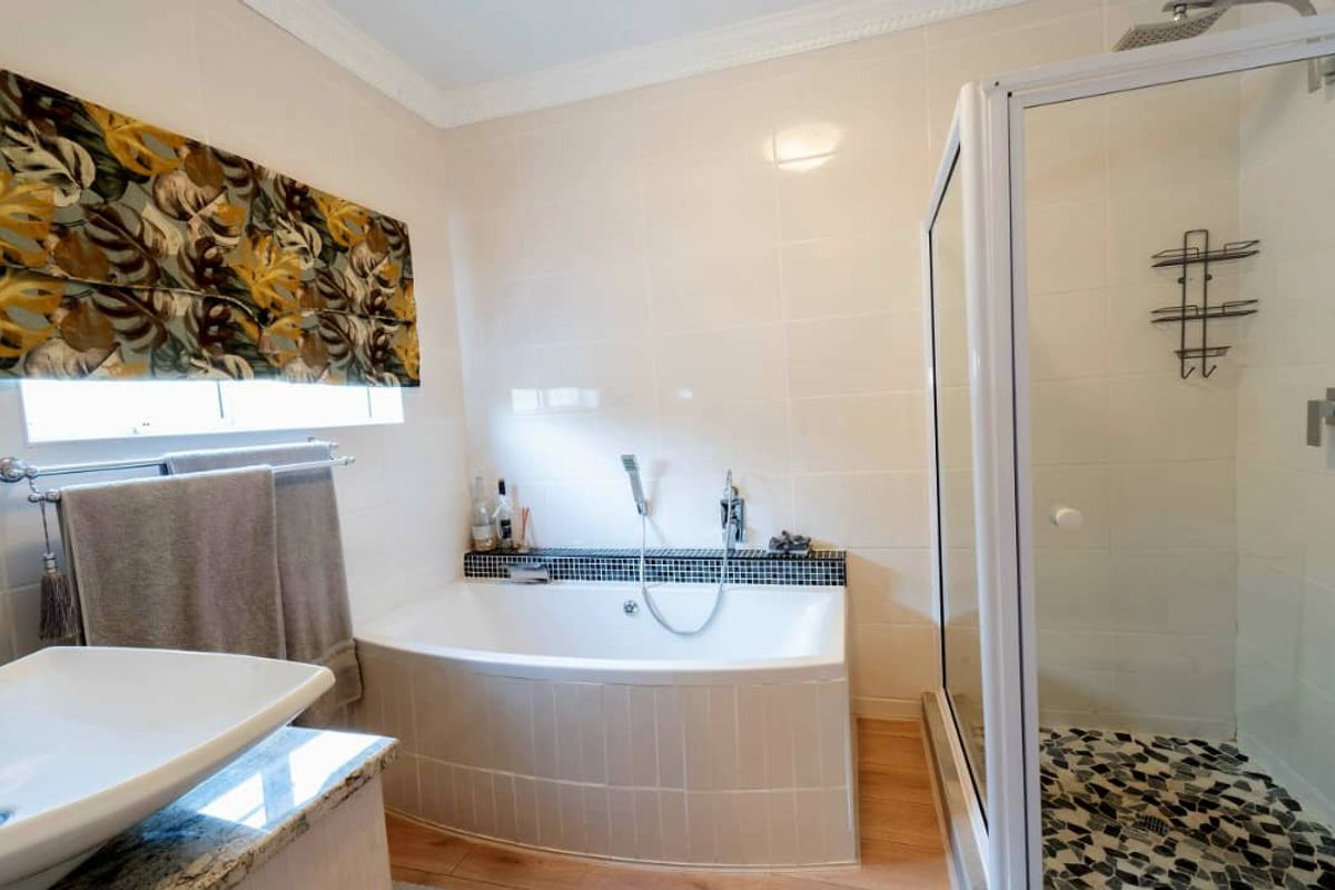 A well-maintained bathroom featuring a built-in bathtub, a separate glass-enclosed shower with pebble-style flooring, and a modern vanity basin.