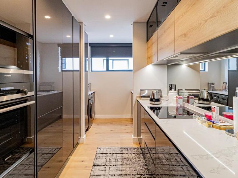 A modern, high-end scullery featuring sleek high-gloss cabinetry, stone countertops, integrated Siemens appliances, and timber flooring, offering a clean and functional prep area.