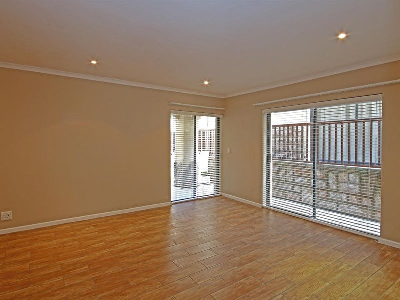 A bright, empty living room featuring tiled flooring, recessed downlights, and large sliding glass doors with venetian blinds providing access to the exterior.