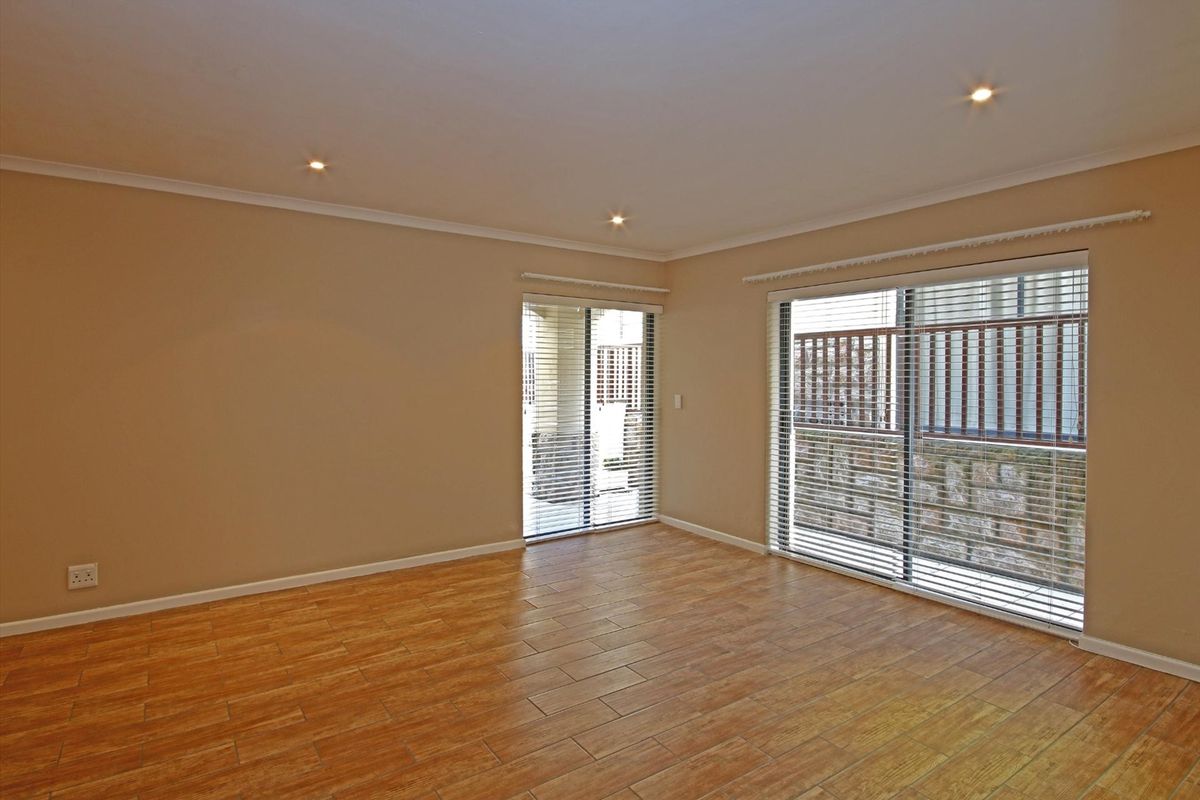 A bright, empty living room featuring tiled flooring, recessed downlights, and large sliding glass doors with venetian blinds providing access to the exterior.