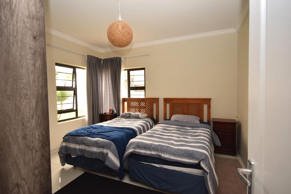 A functional bedroom featuring tiled flooring, cornice detailing, and aluminium window frames, providing a comfortable and well-lit sleeping space.