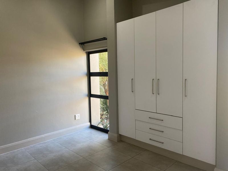 A bright, empty bedroom featuring neutral tiled flooring and a large, modern white built-in wardrobe with integrated drawers.